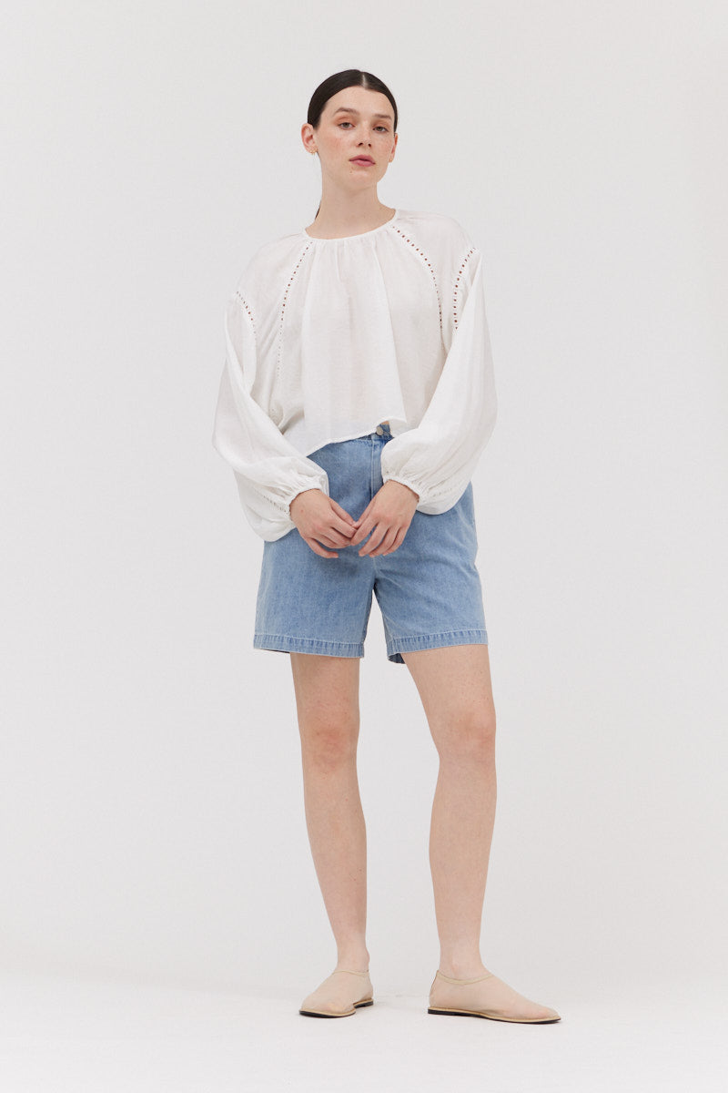 Person wearing a white blouse and blue shorts on a plain background