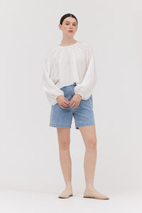 Person wearing a white blouse and blue shorts on a plain background