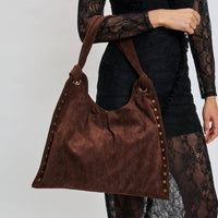 Brown suede handbag with gold studs held by a person wearing a black lace outfit.