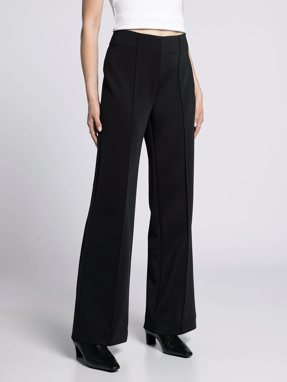 Side view of wide-fit black trousers highlighting sleek tailoring and draped leg.
