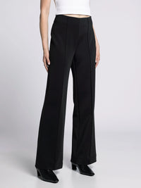 Side view of wide-fit black trousers highlighting sleek tailoring and draped leg.