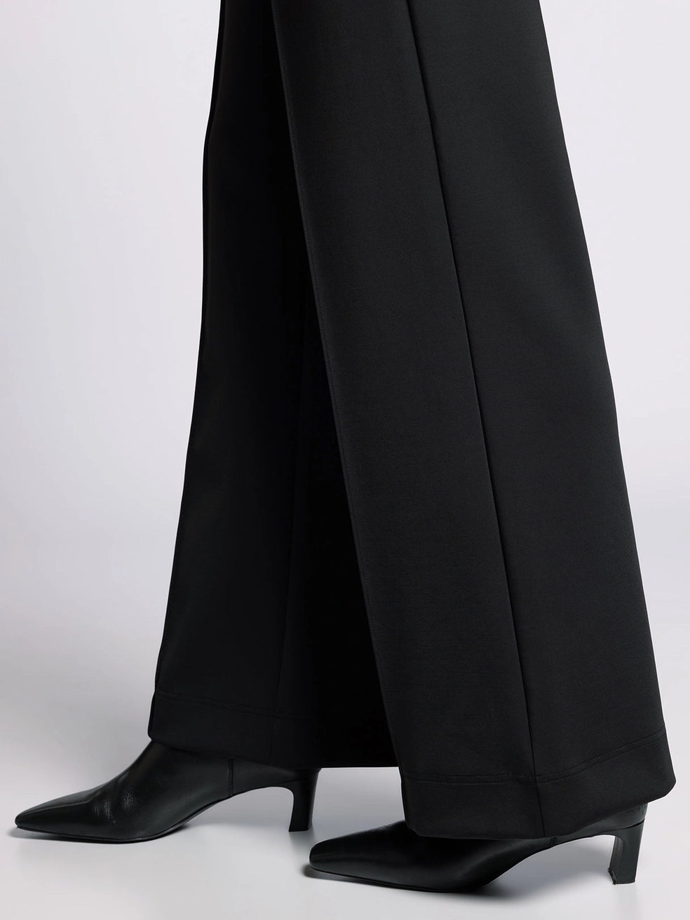 Close-up of black wide-leg pant hem showing structured finish and sleek fabric.