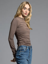 Side view of brown ruched long sleeve top showing stretch fit and gathered sides.