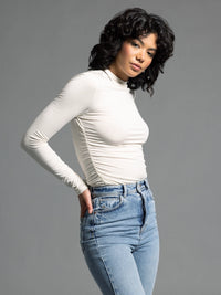 Side view of cream ruched long sleeve top showing sleek fit and stretch texture.