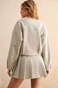 Woman wearing a light gray sweater and pleated skirt against a beige background