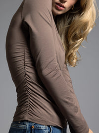 Close-up of ruched detail on brown long sleeve top highlighting stretch fabric.