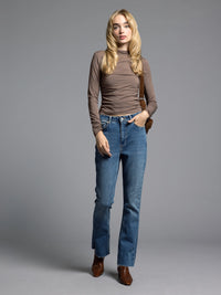 Brown ruched top styled with blue jeans and boots for a modern casual look.