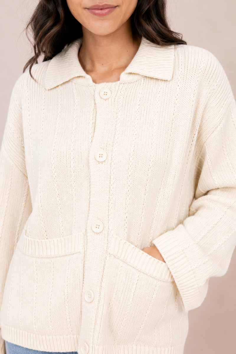A woman wearing a cream-colored ribbed knit cardigan with a collar, front buttons, and front patch pockets, shown against a plain beige background.
