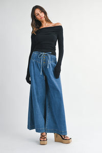 Model wearing the Charlotte Off-Shoulder Ruched Top in black paired with wide-leg denim for a modern chic look.