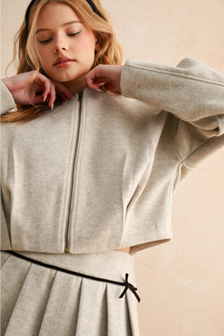 Woman wearing a light gray zip-up jacket over a matching skirt on a beige background