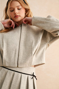 Woman wearing a light gray zip-up jacket over a matching skirt on a beige background