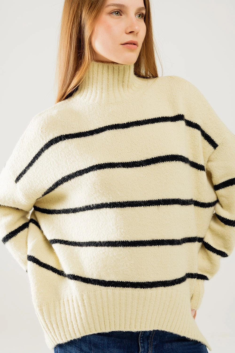 Side view of cozy oversized striped sweater with mock neck and side slits, styled with denim jeans.