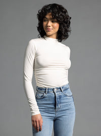Model wearing cream ruched long sleeve top styled with high-waisted light wash jeans.