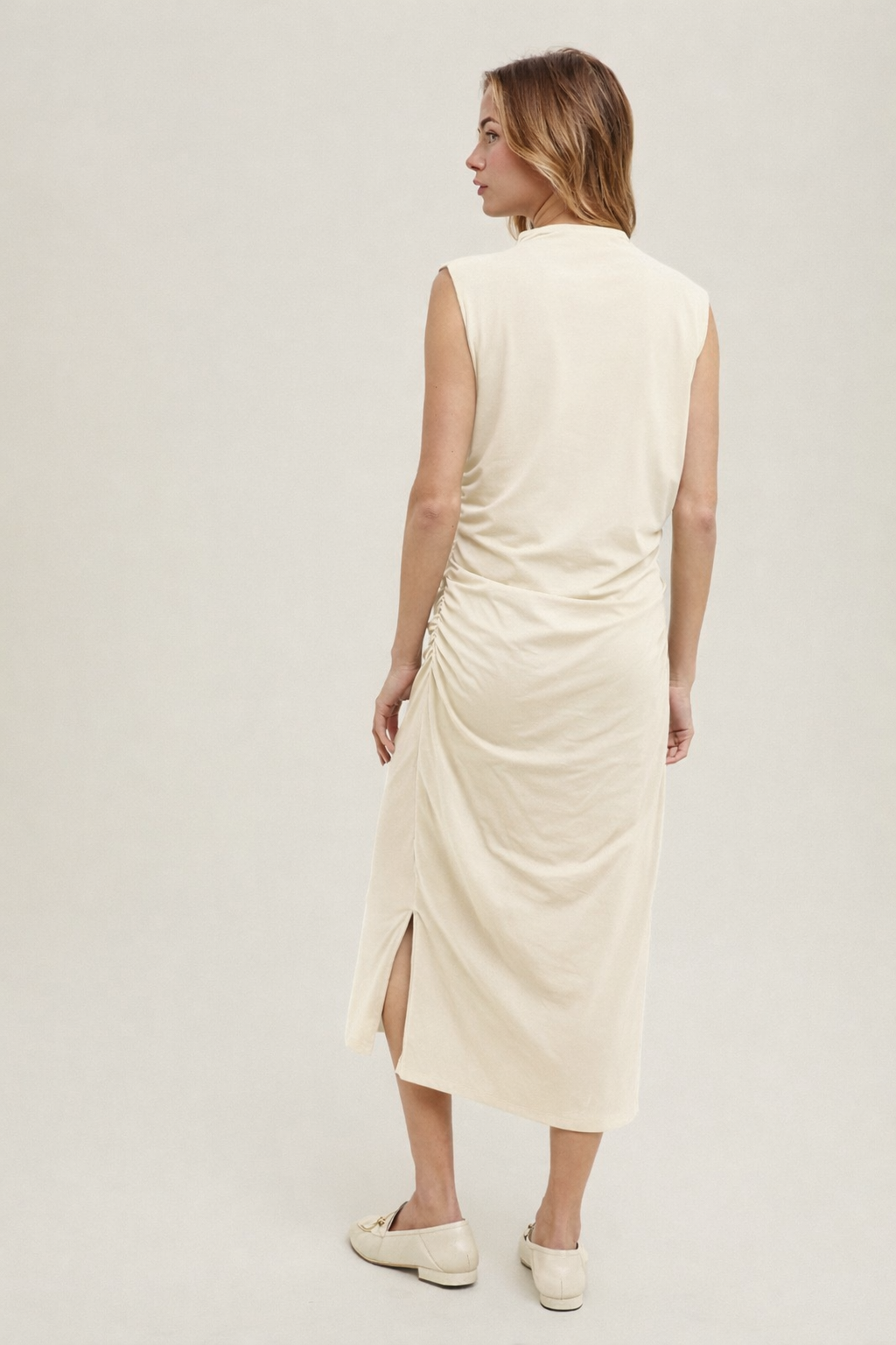 Back view of cream sleeveless ruched midi dress with modern minimalist silhouette