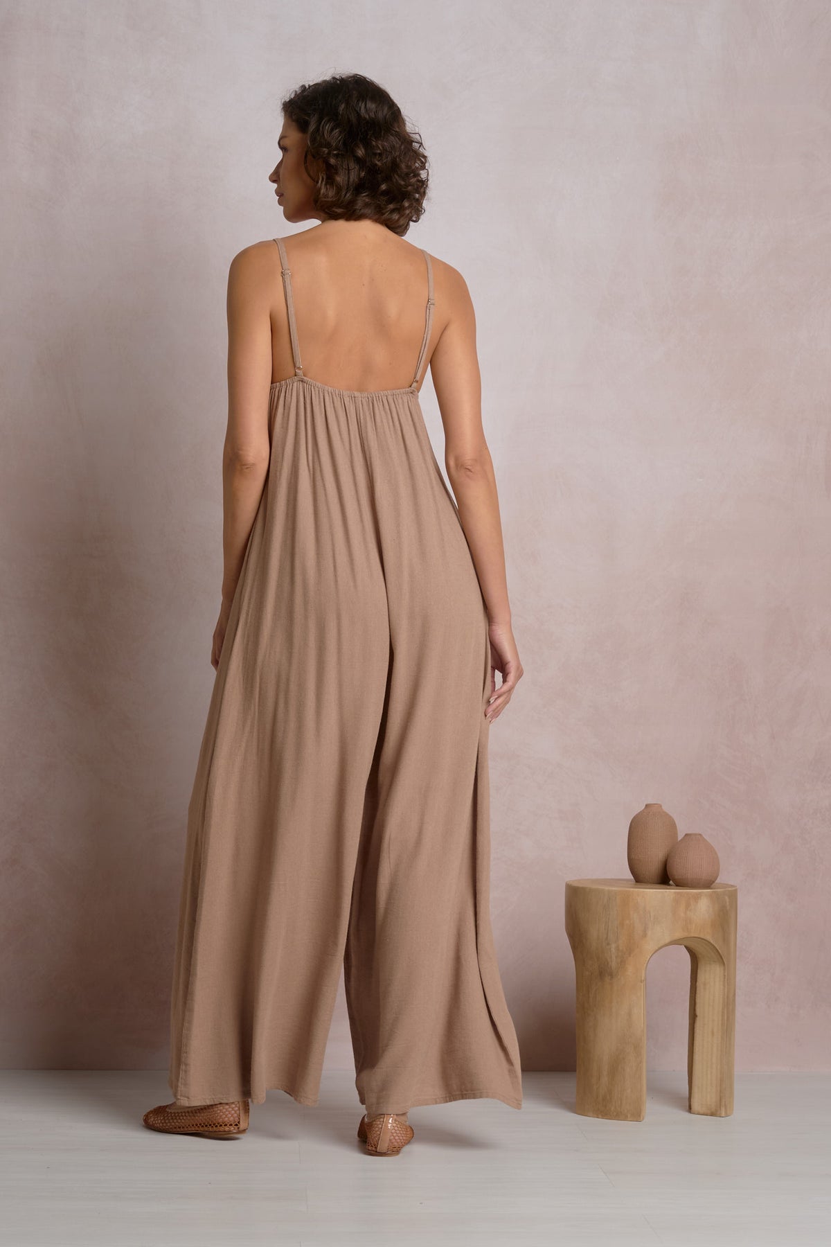 Back view of a model wearing the Courtney wide-leg jumpsuit by Elan in brown, showing the delicate spaghetti straps, gathered back detail, and ultra-relaxed flowy fit.
