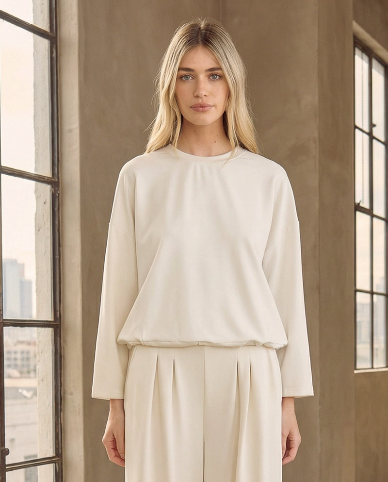 Front view of the luxe white drawstring hem sweatshirt by Reverie. A quiet luxury capsule wardrobe essential styled with matching white pleated wide-leg pants.
