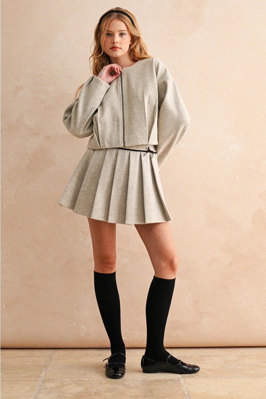 Woman wearing a light gray outfit with a skirt and jacket against a beige background