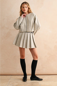 Woman wearing a light gray outfit with a skirt and jacket against a beige background