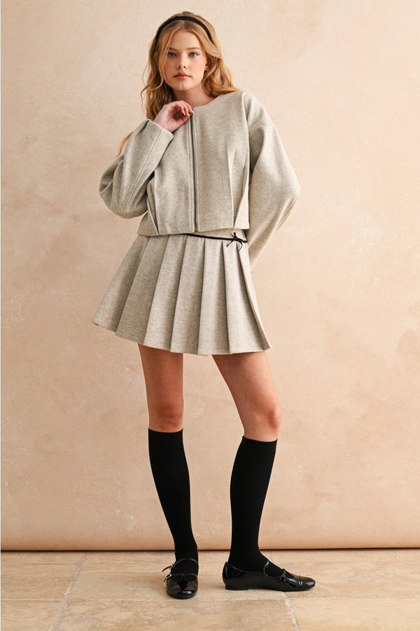 Woman wearing a light gray outfit with a skirt and jacket against a beige background