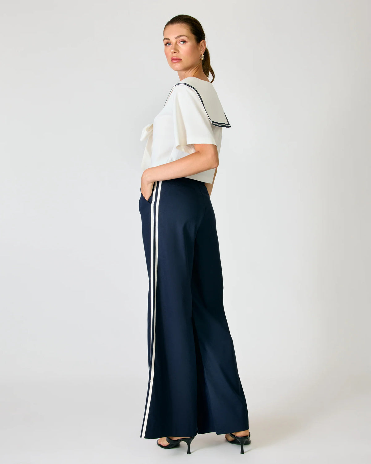 Side profile of a model wearing the Line and Dot Anchor Pants in navy, featuring a white contrast side stripe and wide-leg silhouette, paired with a sailor top
