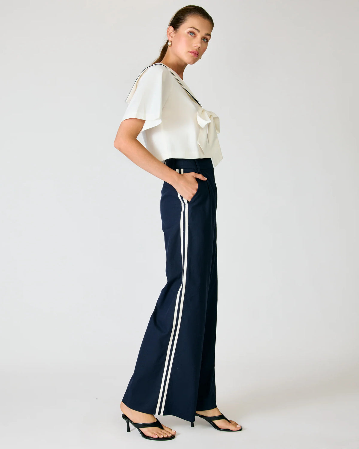 Side profile of a model wearing the Line and Dot Anchor Pants in navy, featuring a white contrast side stripe and wide-leg silhouette, paired with a sailor top.
