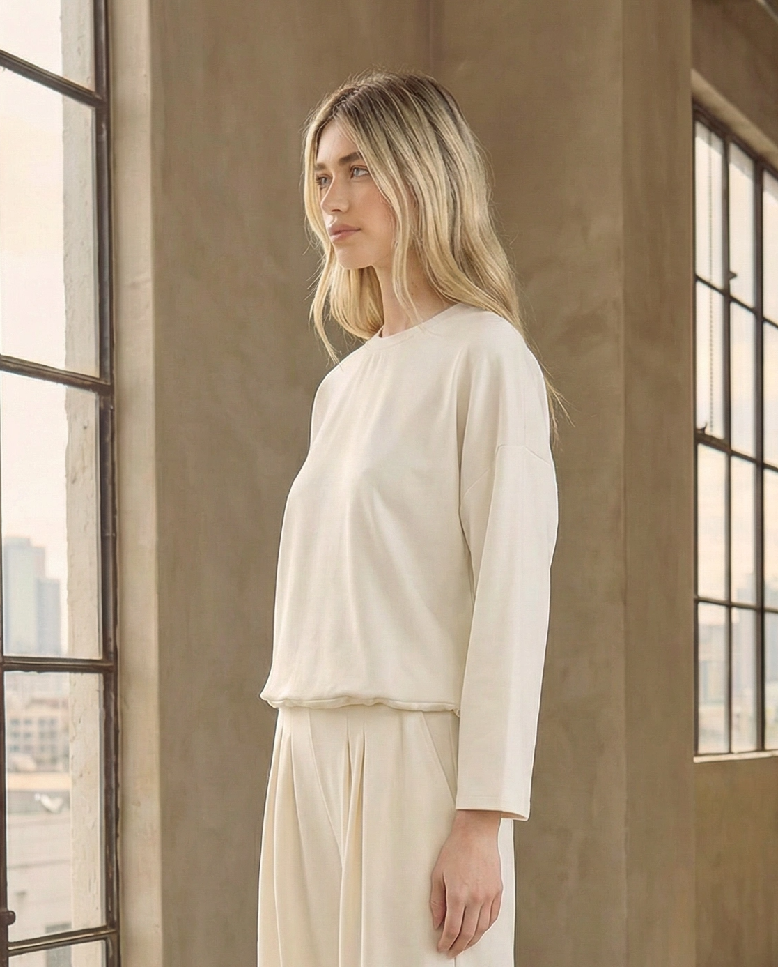 Model wearing the Reverie luxe white crewneck sweatshirt with an adjustable drawstring hem, styled as a matching set with white wide-leg pants and sneakers. Perfect clean aesthetic outfit inspiration.