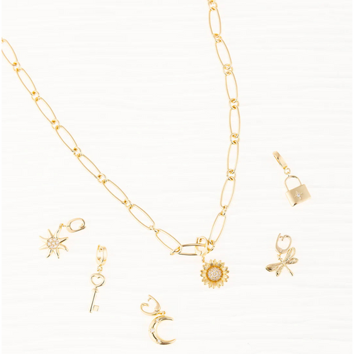A gold paperclip chain necklace styled with various Michelle McDowell symbol charms, including a sun, key, moon, sunflower, dragonfly, and lock charm.