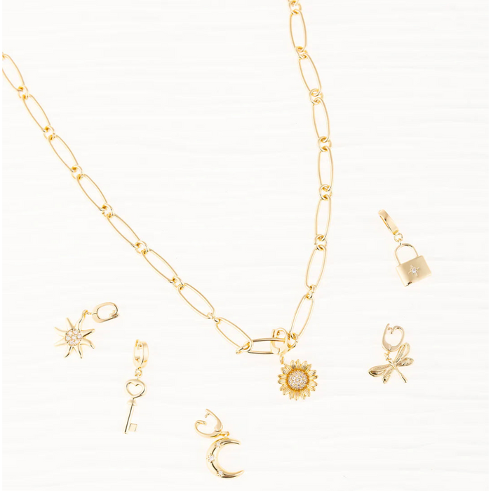 A gold paperclip chain necklace styled with various Michelle McDowell symbol charms, including a sun, key, moon, sunflower, dragonfly, and lock charm.