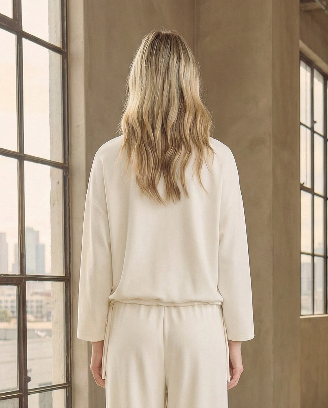 Back view of the minimalist white relaxed-fit sweatshirt from Reverie, showing the clean drop-shoulder design and drawstring waist detail, paired with matching white trousers.