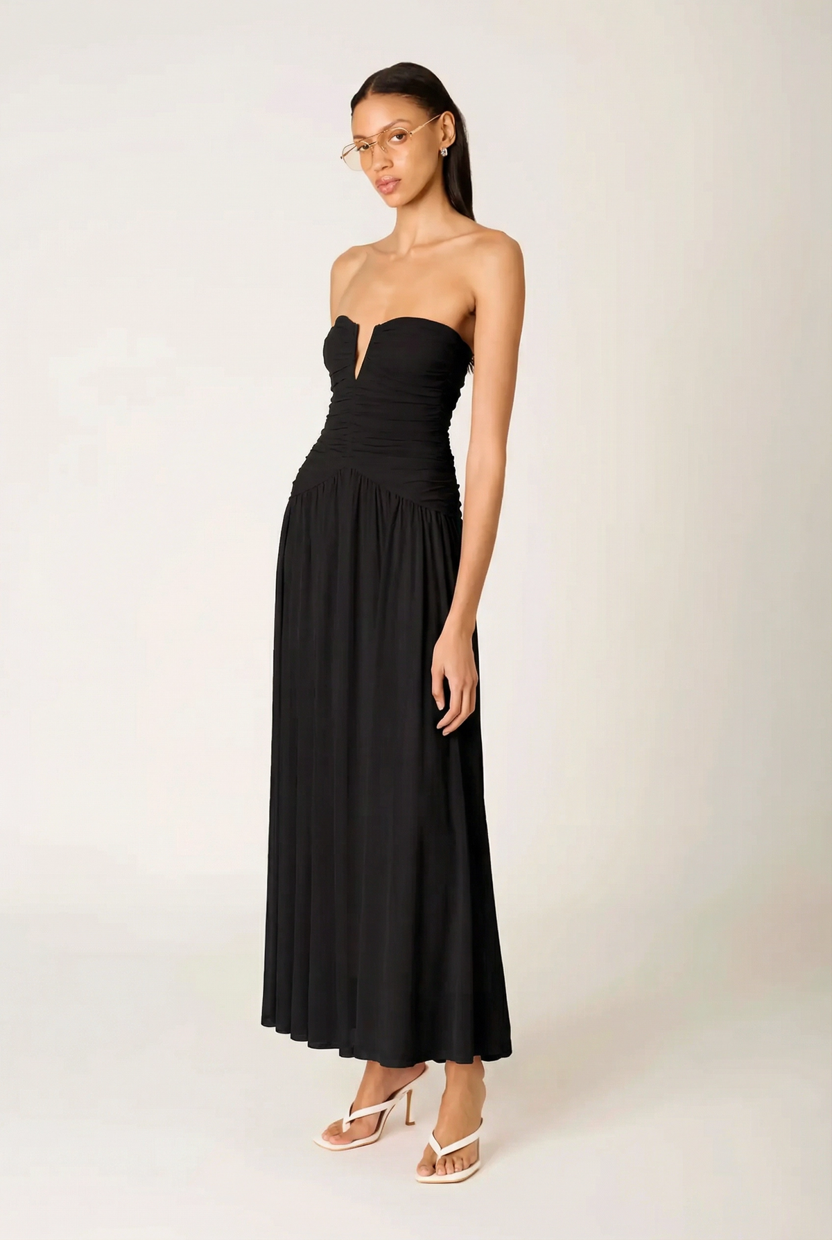 Three-quarter side profile of the NIA Beverly black maxi dress, showing the textured ruching on the bodice and the voluminous gathered skirt.