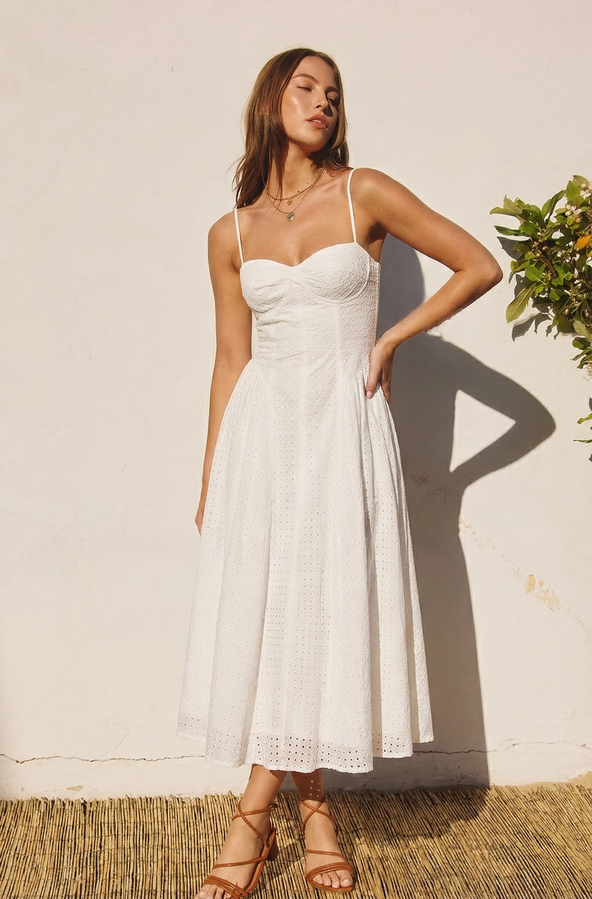 Full body front view of a model wearing the NIA Destene Dress, a white eyelet lace midi dress with a bustier bodice