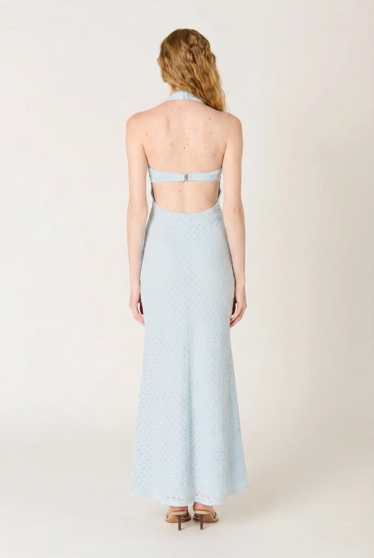 Woman wearing a light blue halter neck dress with open back on a white background
