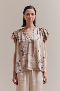 Model wearing the Perry Ruffle Sleeve Blouse in beige satin floral print — soft neutral blouse with flutter sleeves.