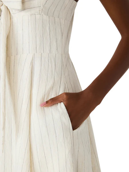 Close-up of a person wearing a white pleated dress with a hand on the hip against a white background