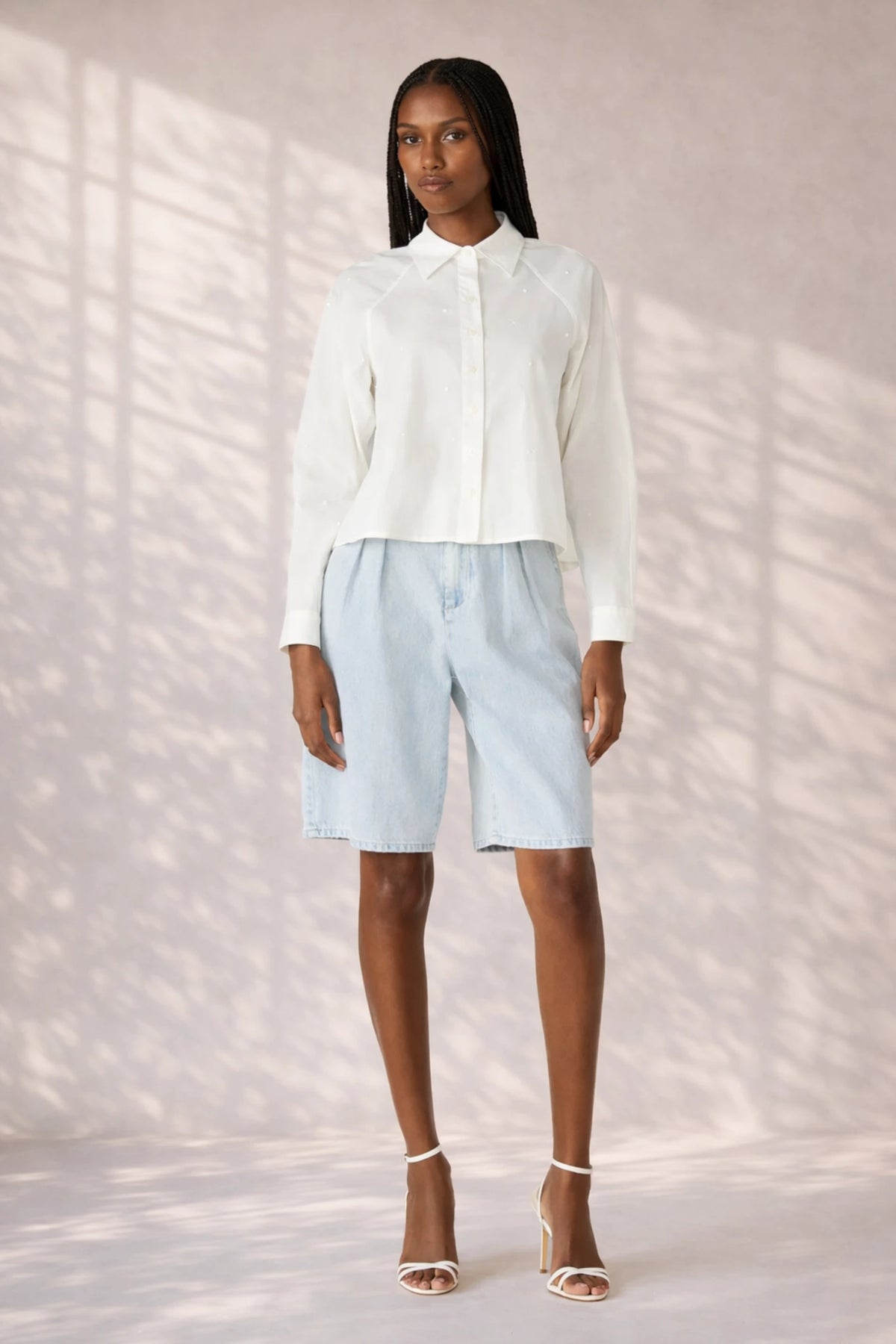 Woman wearing a white blouse and light blue shorts against a neutral background