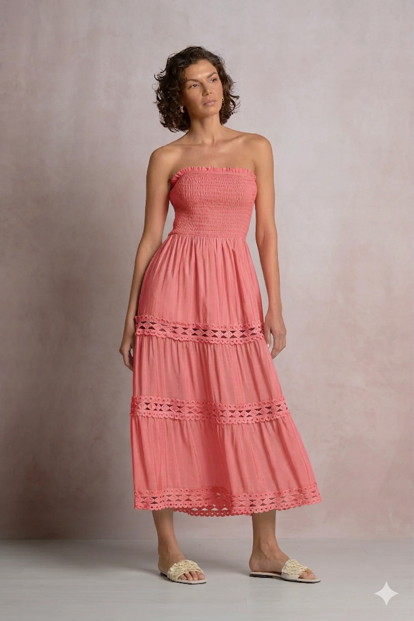 A woman modeling a vibrant coral strapless summer maxi dress with a flattering smocked bodice and three-tiered skirt with crochet lace inserts, perfect for resort wear or boutique summer fashion.