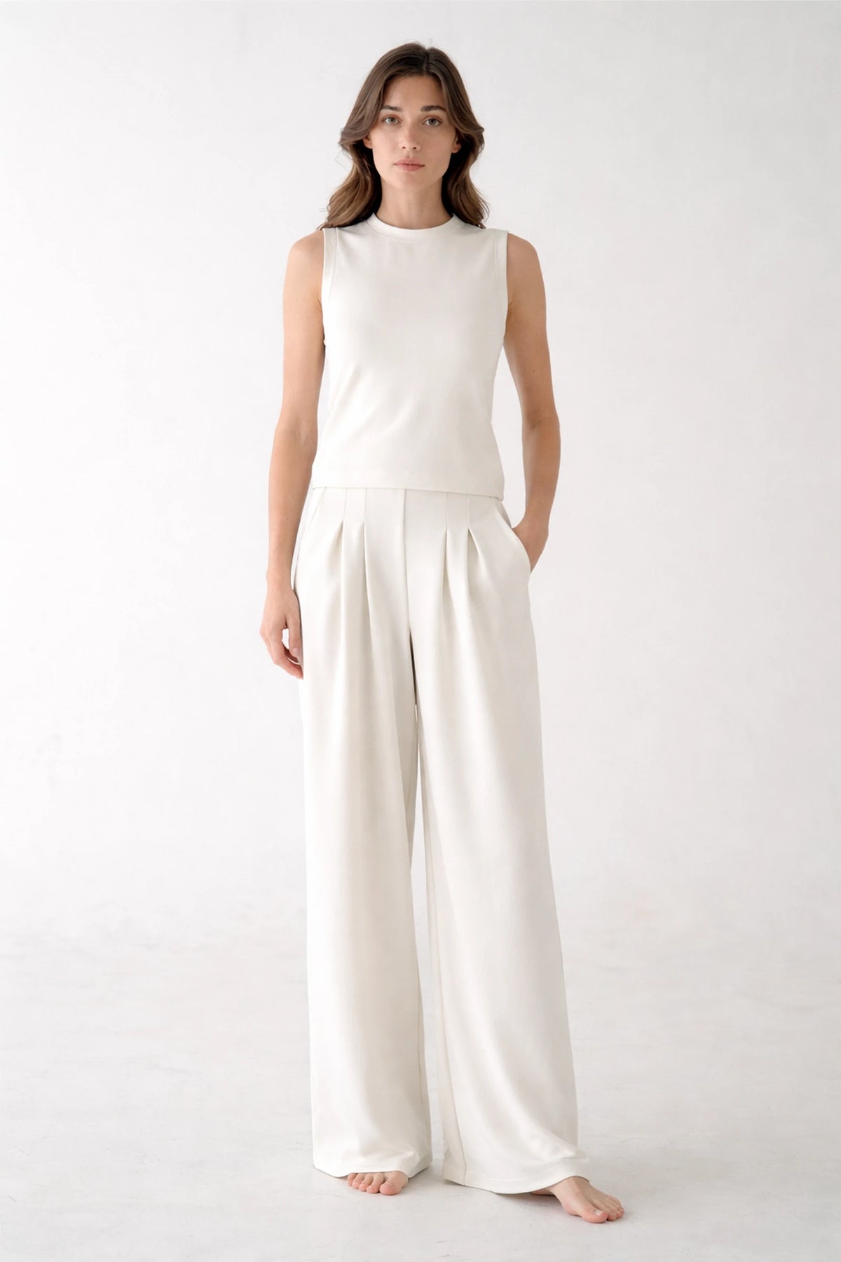 Front view of a woman wearing high-waisted white pleated wide-leg sweatpants, showing the tailored trouser look and relaxed fit.