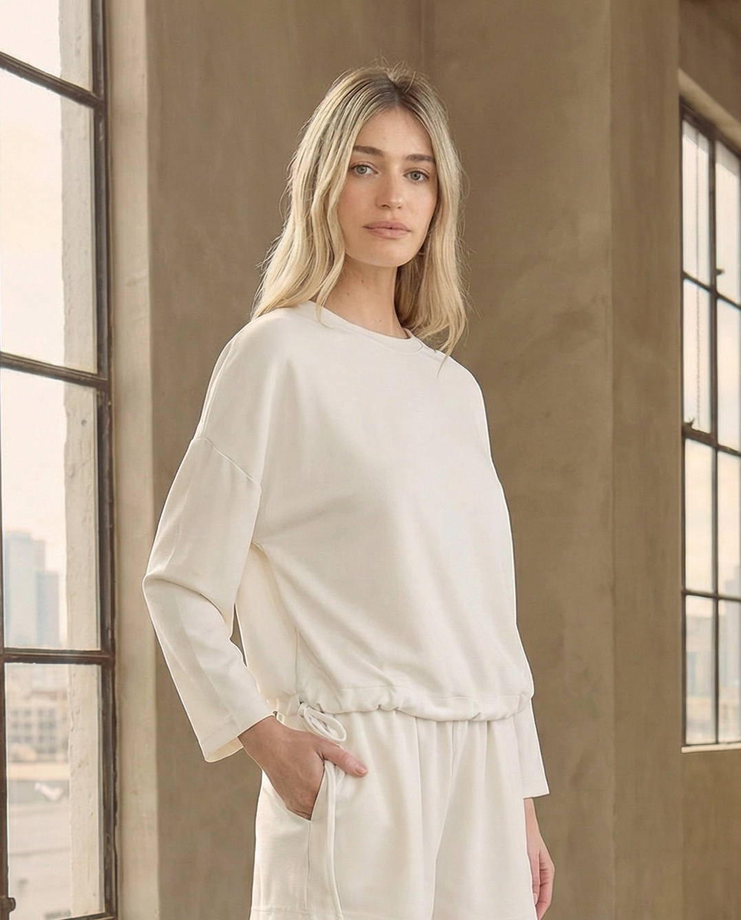 Model styling the Reverie luxe white drawstring sweatshirt with matching white lounge shorts. A chic, comfortable monochromatic outfit perfect for travel or weekend wear.