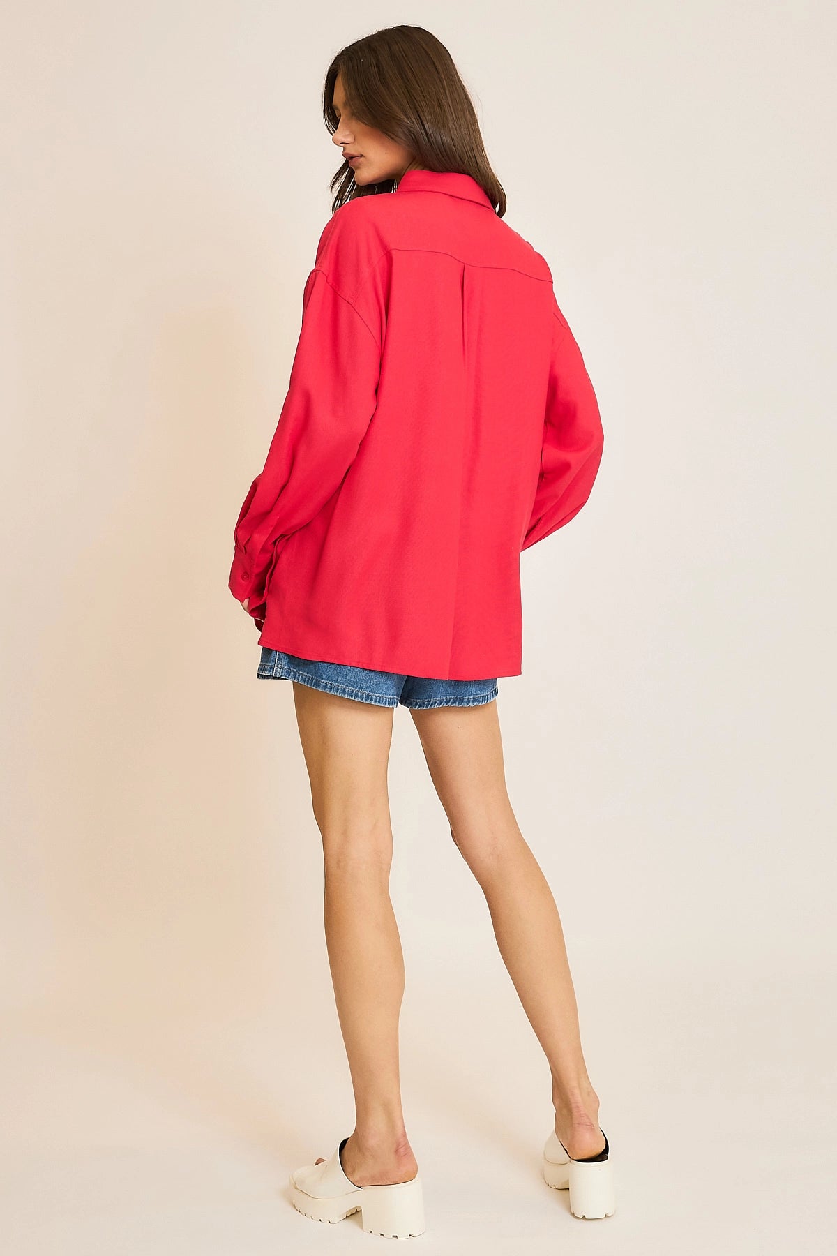 Person wearing a red jacket and denim shorts on a beige background