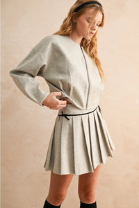 Woman wearing a light gray outfit with a skirt on a beige background